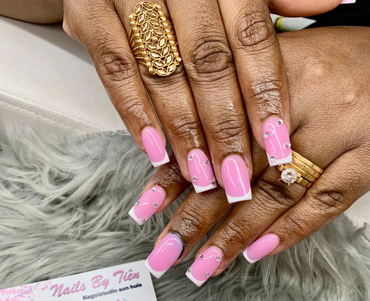 Roze nagels met een witte French en kleine steentjes, op een grijs vachtje