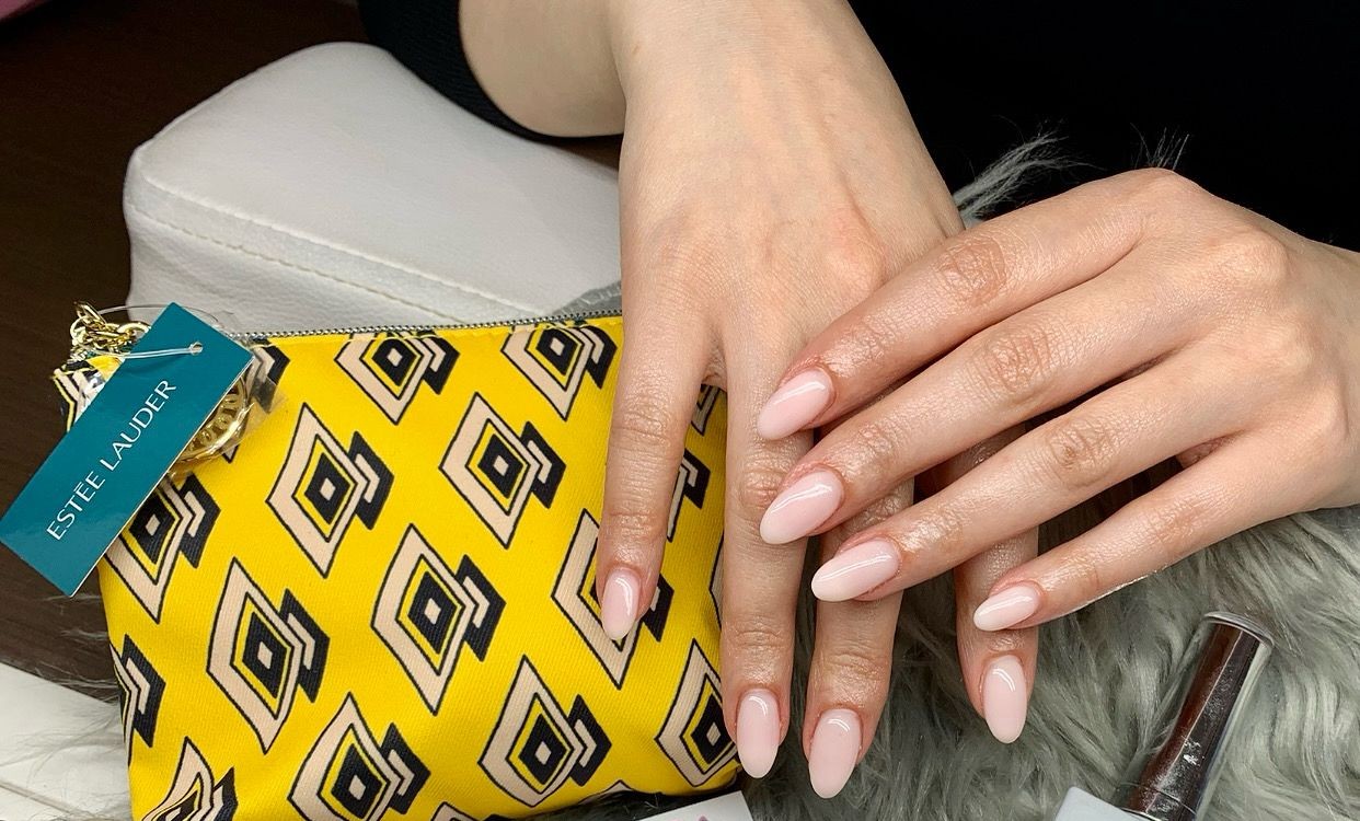 Zacht roze amandelvormige nagels naast een flesje nagellak
